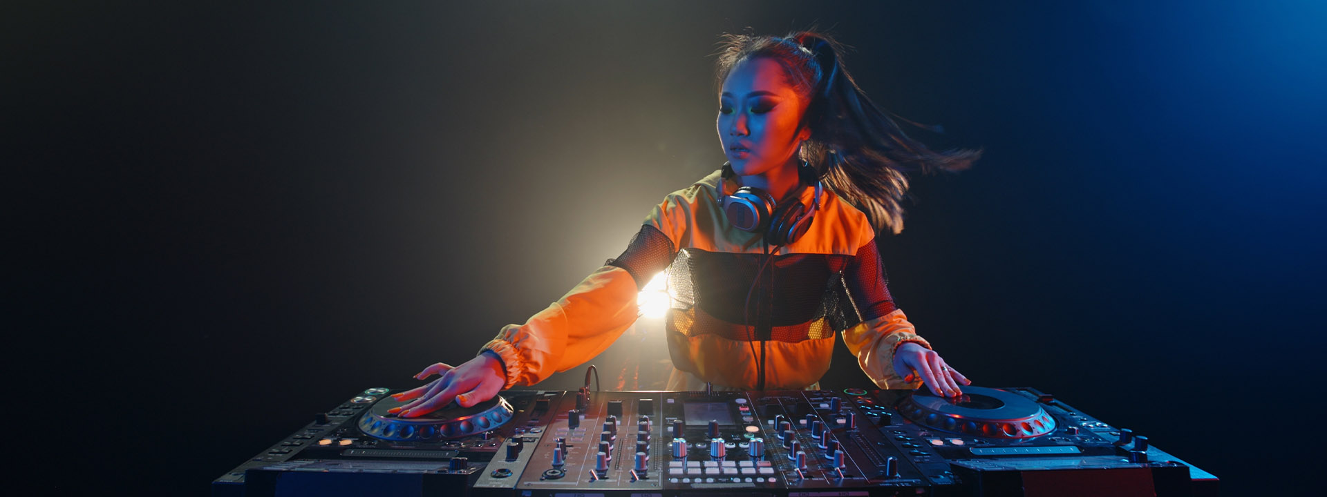 DJ performing to a crowd at an outdoor event, surrounded by trees and snow. People are watching and some are taking photos.