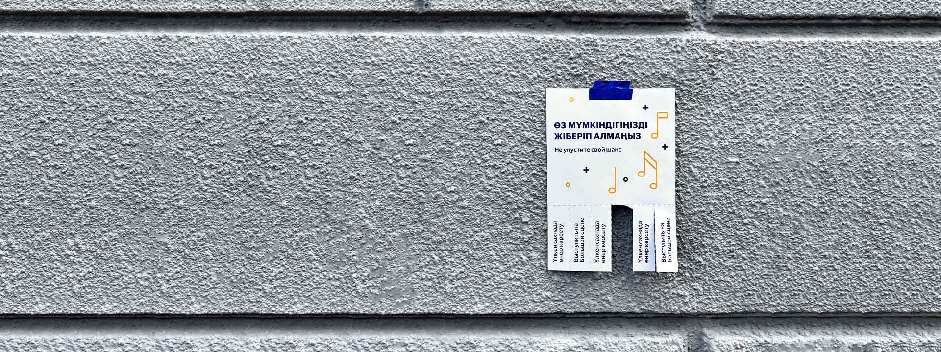 A poster with pull-off tabs is taped to a textured grey wall with blue tape. The poster advertising a music lesson is partially written in a non-English language.