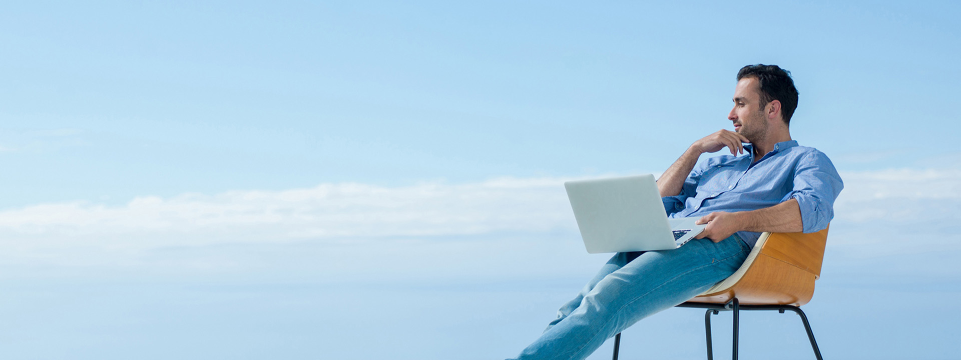 A man with a laptop sitting on the chair near the sea shore