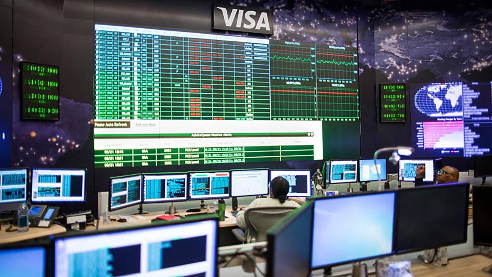 A person is in the visa data center control room and follows the data monitors