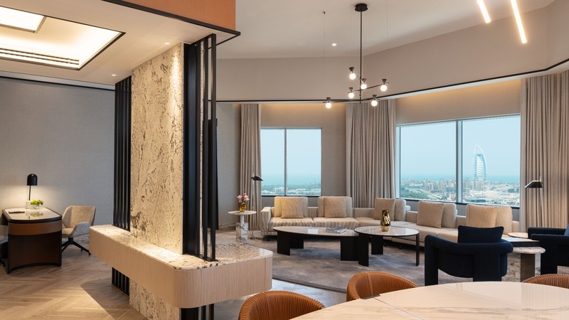 Spacious modern living room with large windows, contemporary furniture, decorative lighting, and a view of a cityscape with a prominent tower in the background.