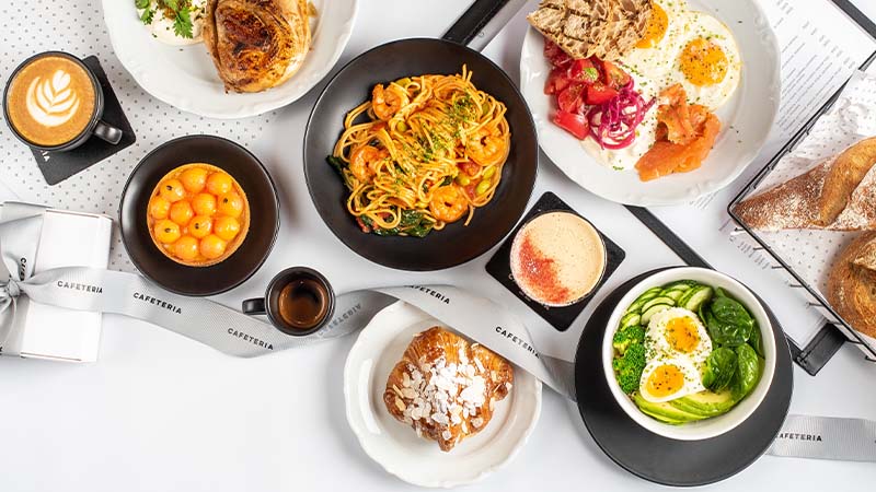 A table with various dishes including pasta, eggs with avocado, smoked salmon, pastries, fruit, and cups of coffee and espresso.