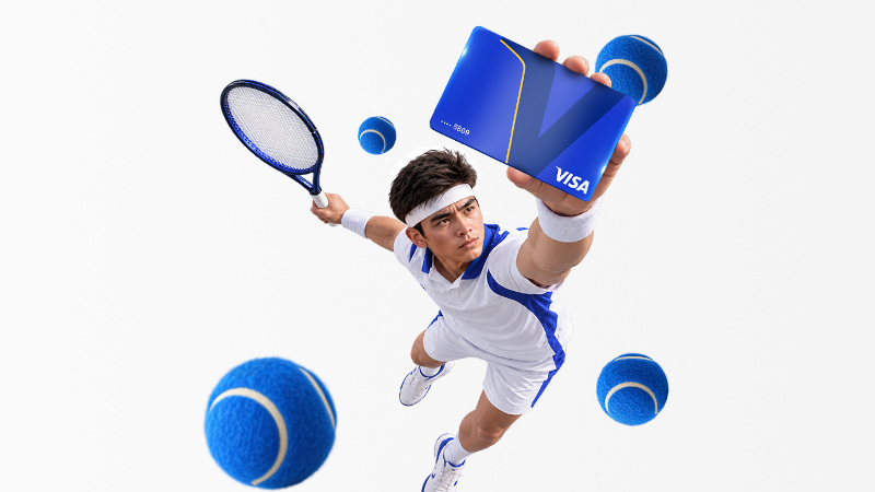 A tennis player in a white uniform reaches forward to hold up a blue Visa credit card, surrounded by floating tennis balls and a racket.