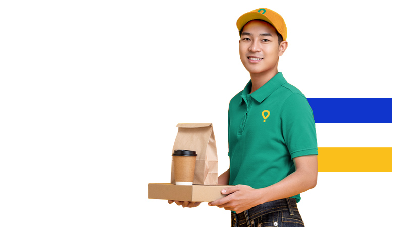 Smiling delivery person in a green uniform holds a tray with a coffee cup and paper bag.
