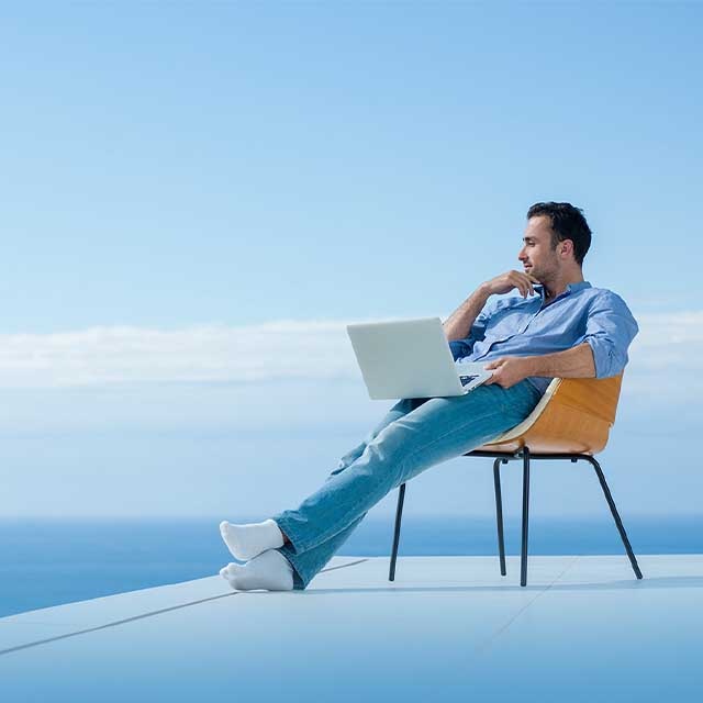 A man with a laptop sitting at the seaside