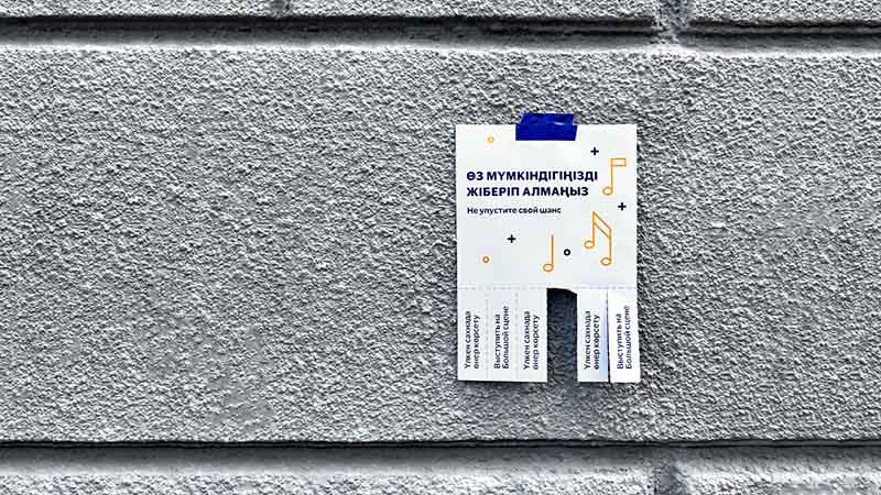 A poster with pull-off tabs is taped to a textured grey wall with blue tape. The poster advertising a music lesson is partially written in a non-English language.